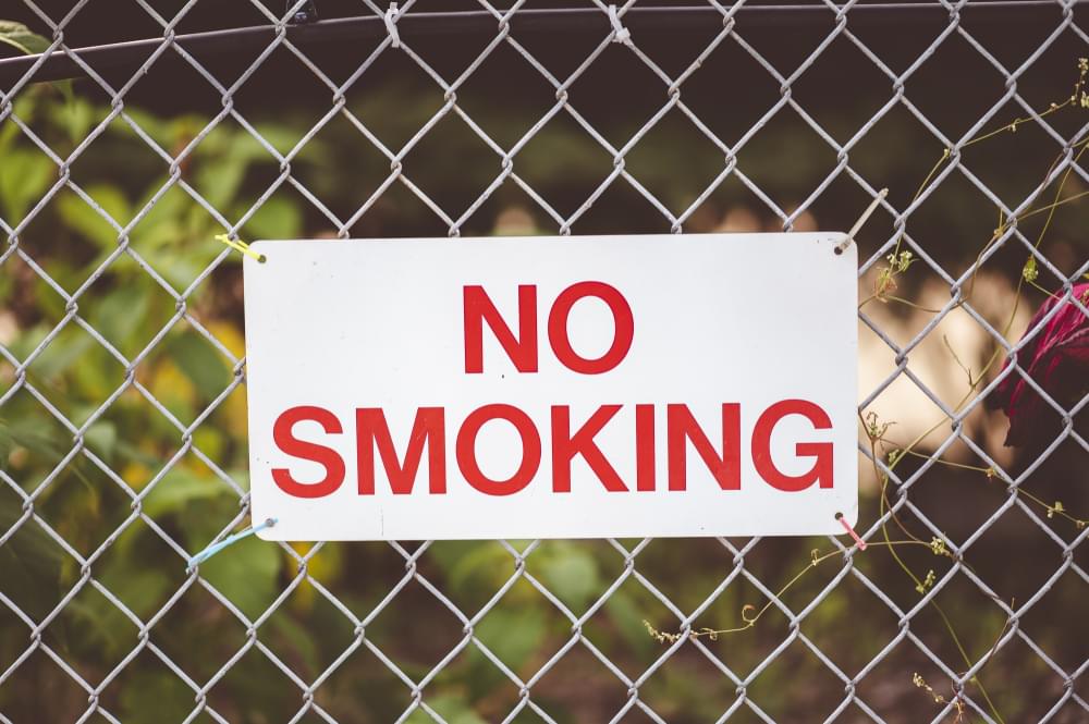 Closeup-focus-shot-of-no-smoking-sign-hanging-by-the-fence.jpg