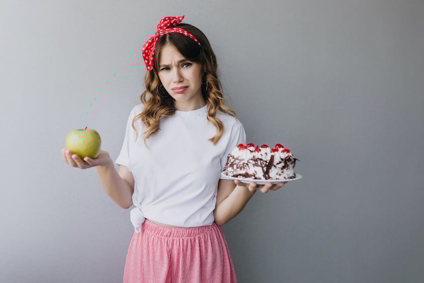 Slim-sad-girl-holding-fruits-and-cake-charming-curly-female-model-can-t-decide-what-to-eat-1.jpg