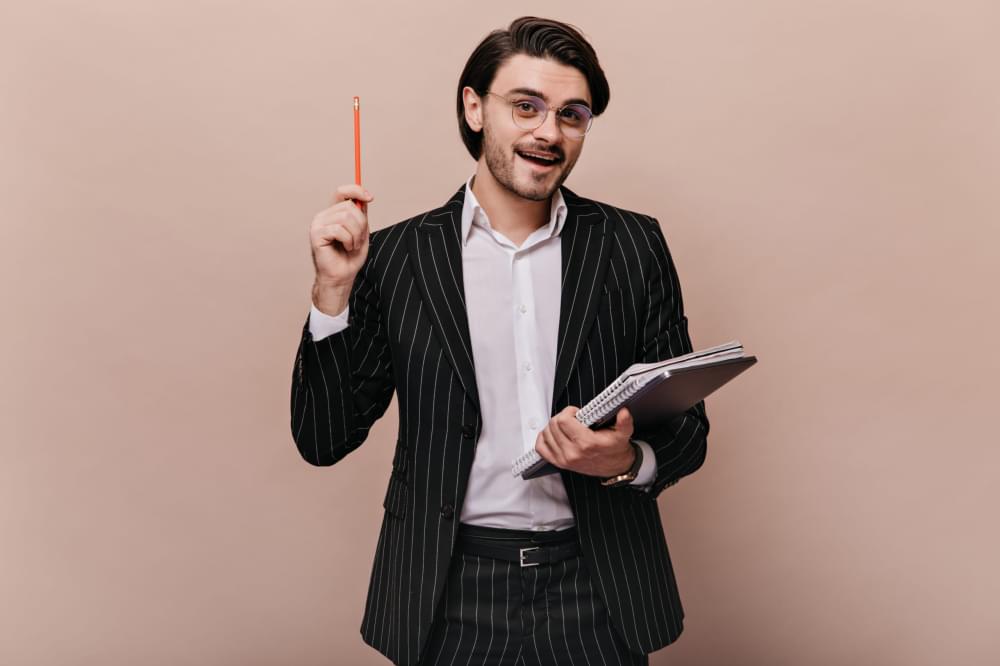 Elegant-young-teacher-with-brunette-hair-in-stylish-light-shirt-black-striped-suit-glasses-holding-writings-pen-and-giving-lecture-scaled-1.jpg